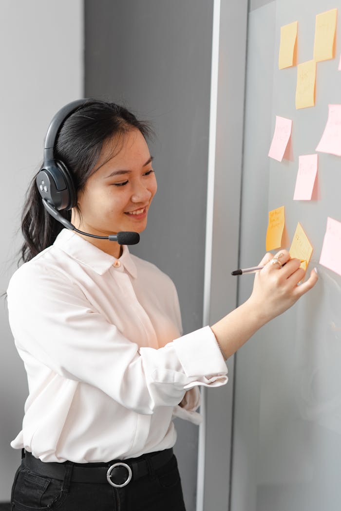 Smiling call center agent wearing headset, writing notes in office.
